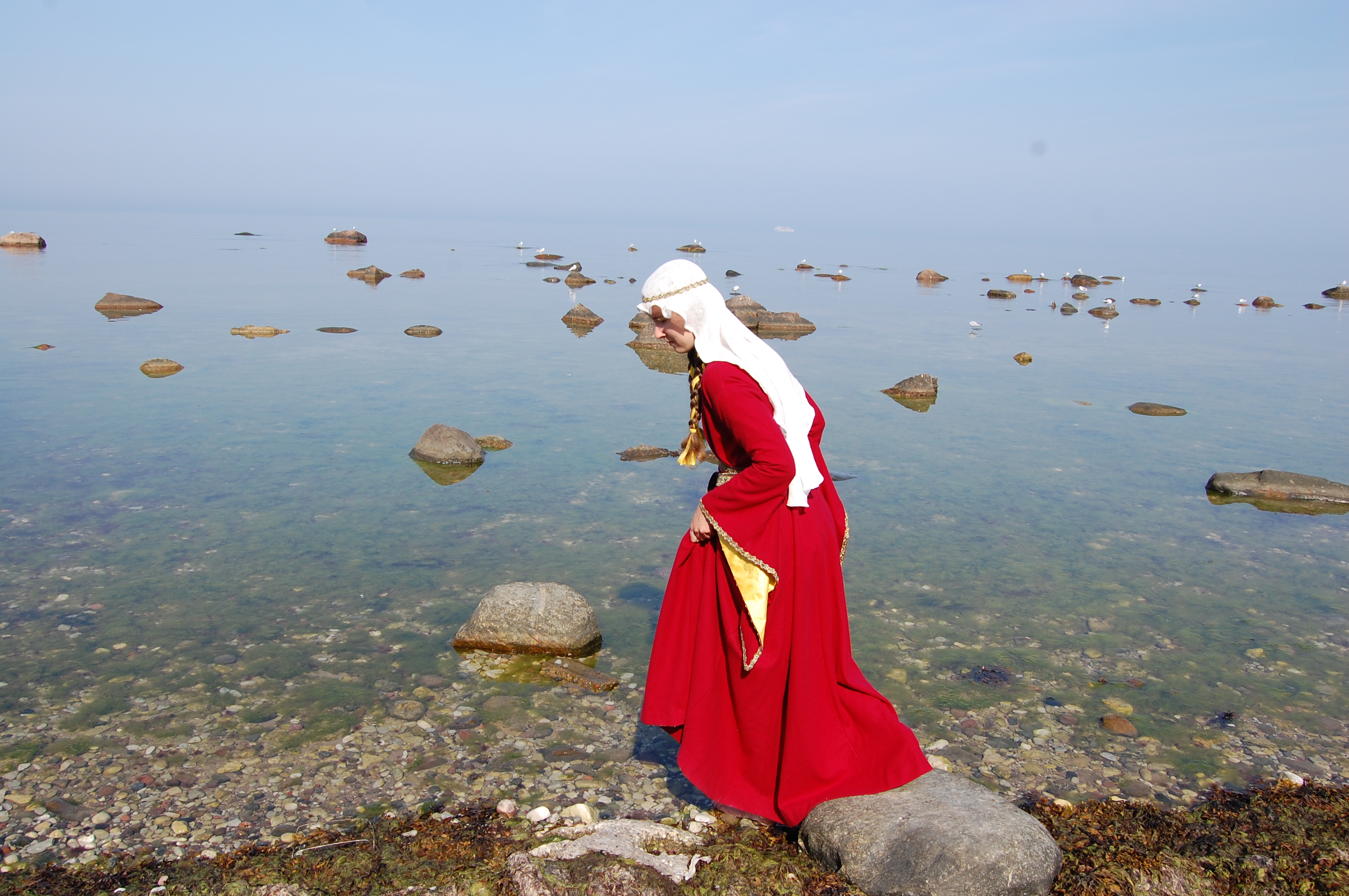 Vadar i havet i röd medeltidsklänning och slöja.
